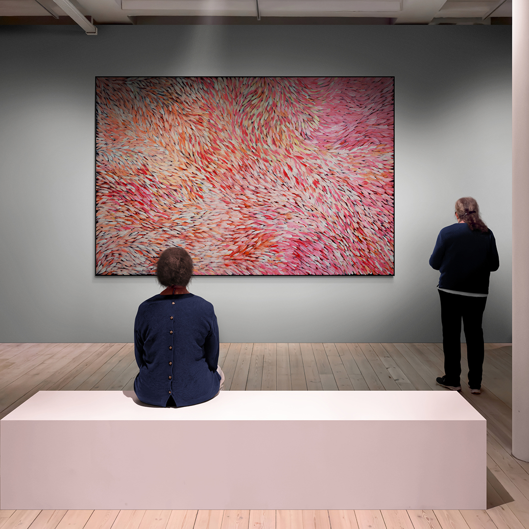 A large painting by Gloria Petyarre hanging in a gallery with people admiring it.