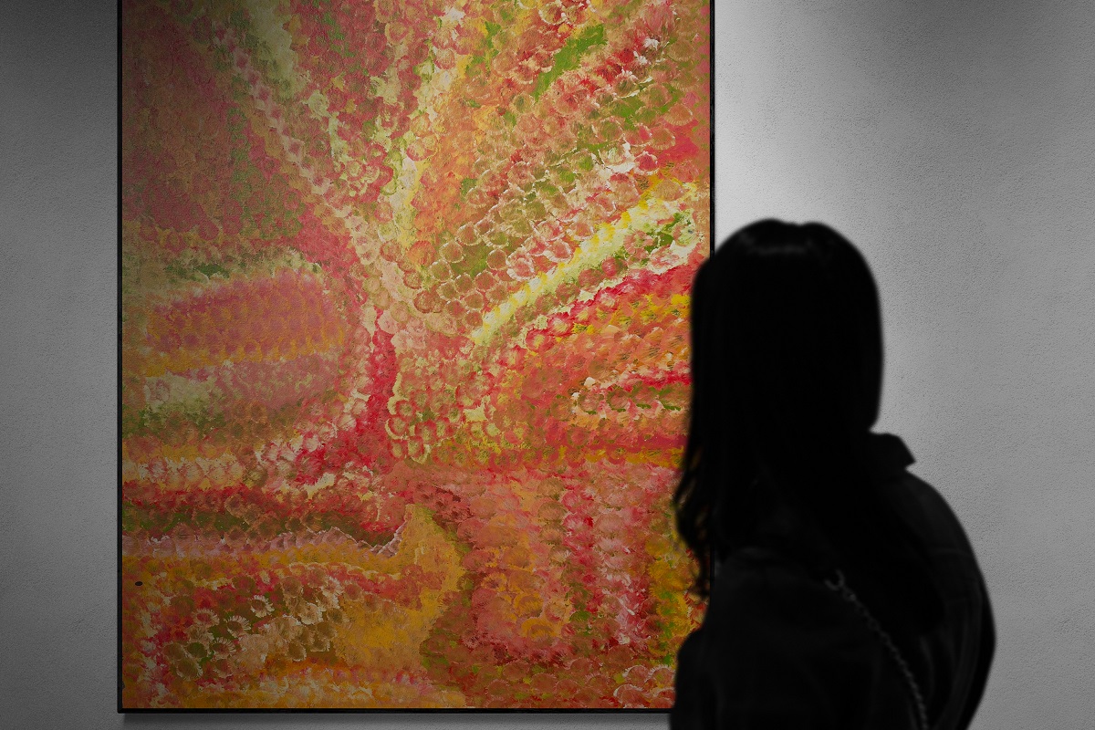 Silhouette of a woman looking at a spotlit painting by Emily Kame Kngwarreye